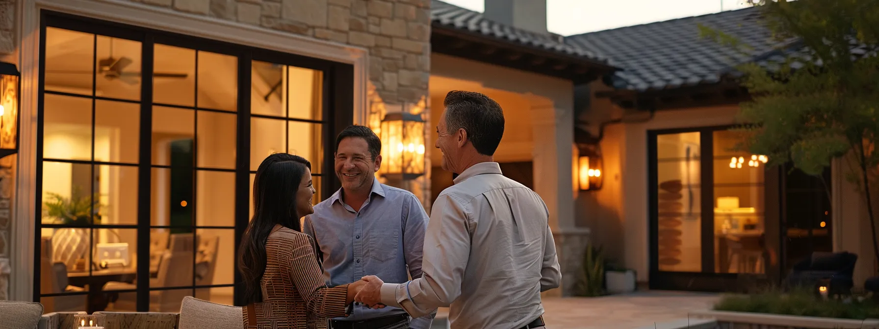 a couple smiling and shaking hands with a reputable home builder in front of a beautiful custom-designed model home.